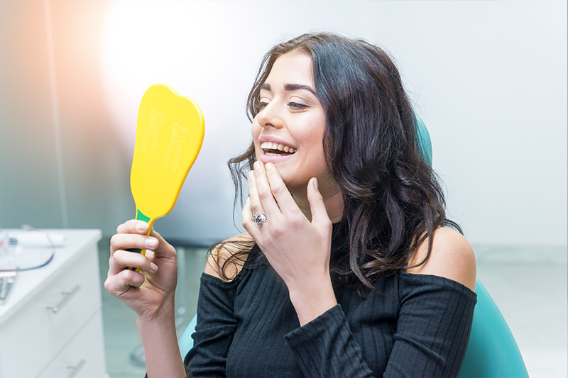 Patient checking her smile in the mirror after treatment at Avenue Dentistry